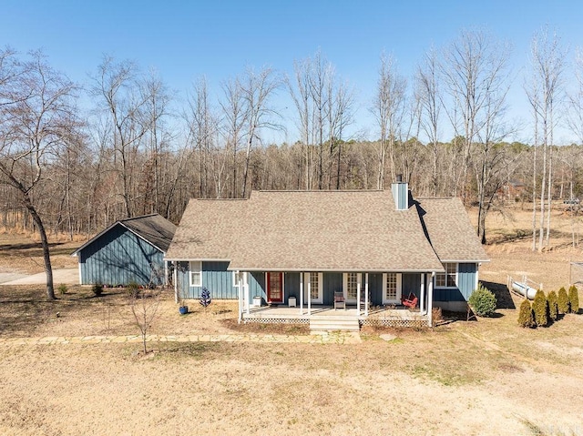 view of front of property with board and batten siding, roof with shingles, a porch, and a chimney