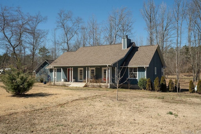 view of front of home with roof with shingles, a porch, a chimney, and a front lawn