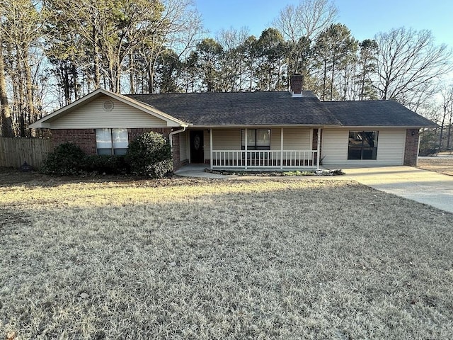 ranch-style house featuring brick siding, a chimney, covered porch, fence, and a front yard