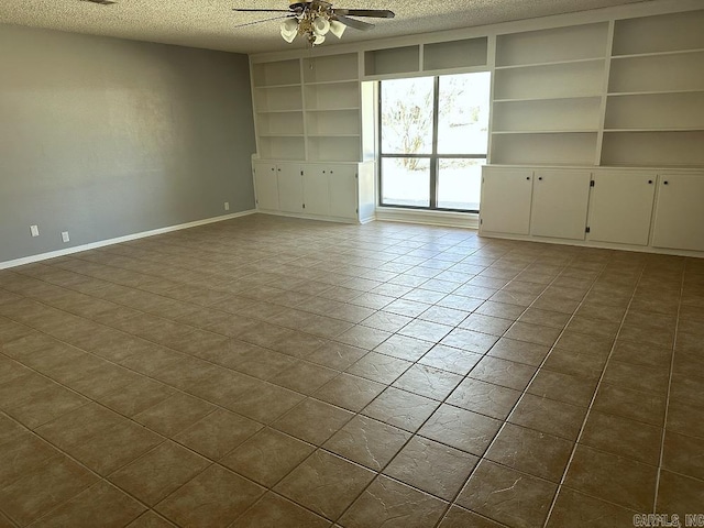 spare room with a textured ceiling, ceiling fan, built in shelves, tile patterned flooring, and baseboards