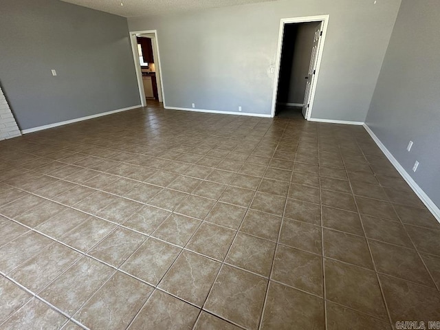 spare room featuring a textured ceiling, tile patterned floors, and baseboards