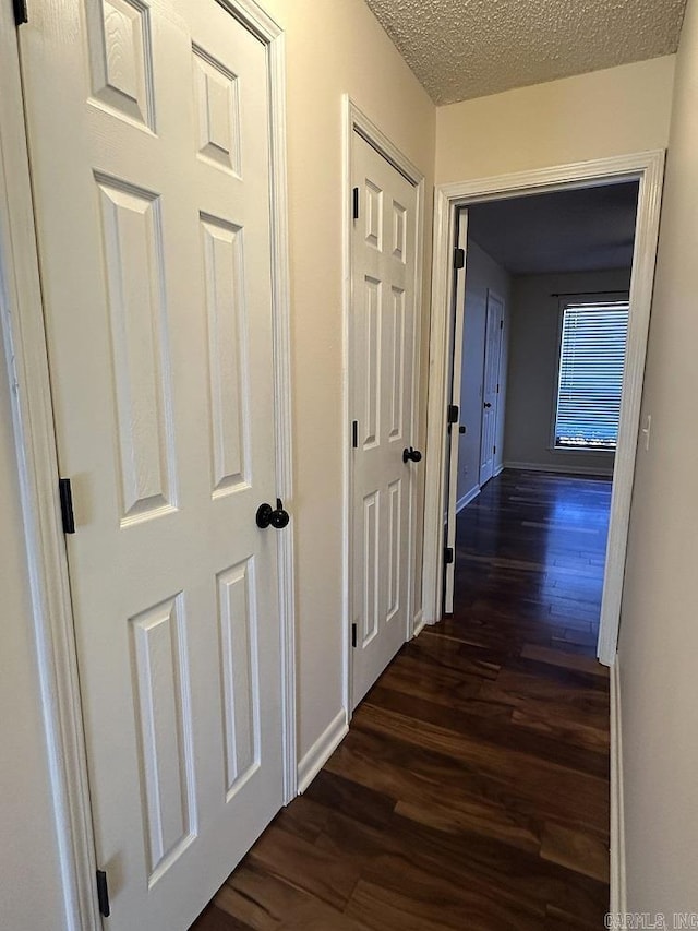 hallway with a textured ceiling, baseboards, and dark wood-type flooring