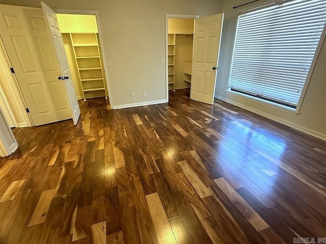 unfurnished bedroom featuring a closet, dark wood finished floors, a spacious closet, and baseboards