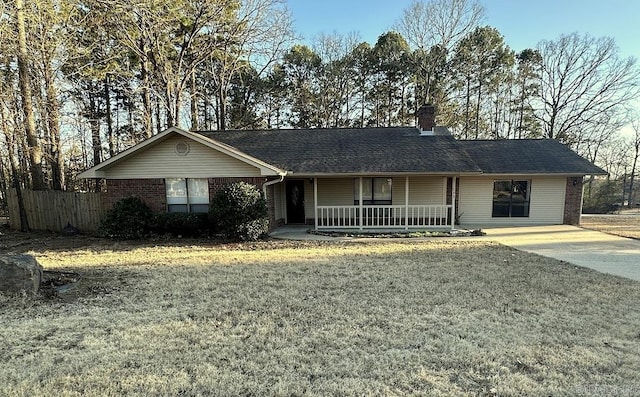 ranch-style house with brick siding, roof with shingles, a chimney, covered porch, and a front yard