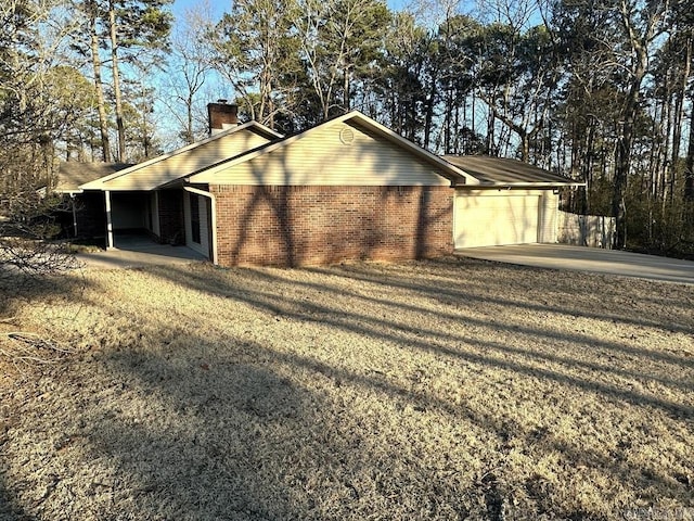 view of side of property featuring an attached garage, a chimney, concrete driveway, and brick siding