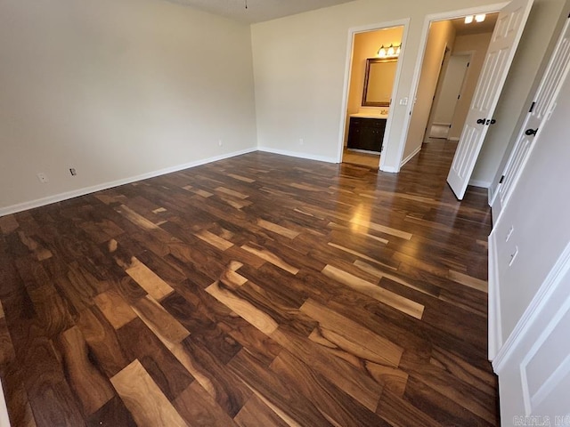 unfurnished bedroom featuring connected bathroom, baseboards, and dark wood-type flooring