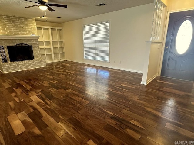 unfurnished living room with a brick fireplace, a textured ceiling, visible vents, and dark wood-style flooring