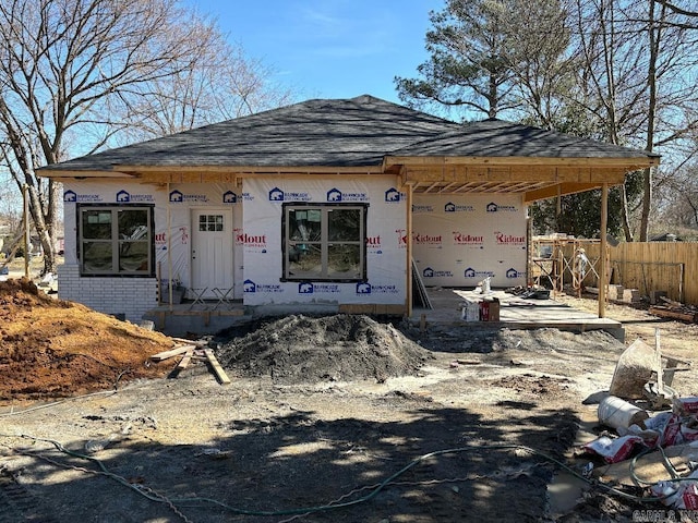 unfinished property with brick siding, fence, and roof with shingles