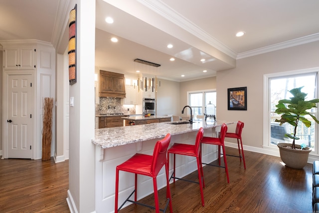 kitchen with tasteful backsplash, dark wood-style floors, a breakfast bar area, ornamental molding, and a sink