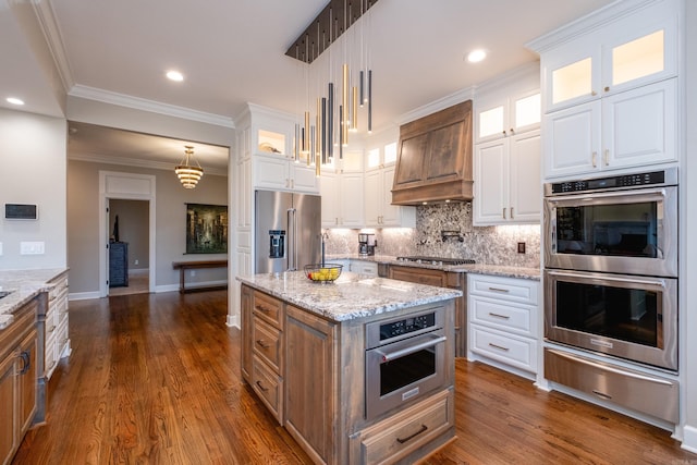 kitchen with a warming drawer, stainless steel appliances, decorative backsplash, white cabinets, and premium range hood