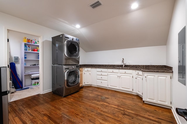 laundry room with stacked washer / drying machine, dark wood finished floors, visible vents, and cabinet space