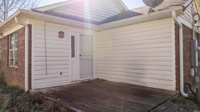 doorway to property featuring brick siding, roof with shingles, and a wooden deck