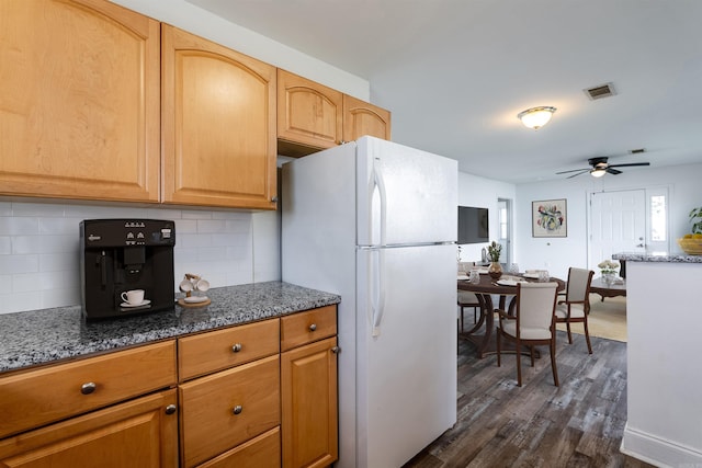 kitchen with stone countertops, freestanding refrigerator, visible vents, and ceiling fan