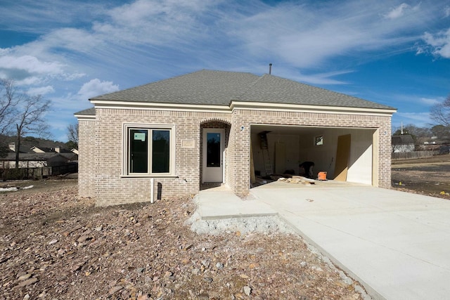 view of front of house featuring driveway, a shingled roof, an attached garage, and brick siding