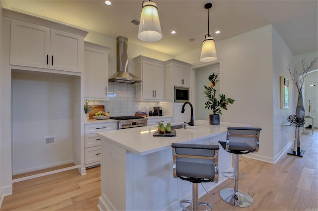 kitchen featuring light countertops, stainless steel microwave, backsplash, a sink, and wall chimney range hood