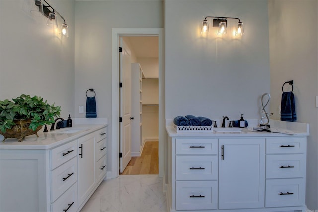 full bathroom with marble finish floor, two vanities, a sink, and a spacious closet