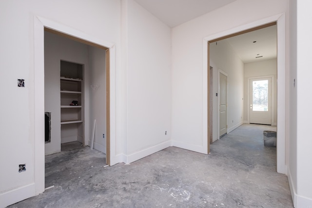 corridor featuring concrete flooring and baseboards