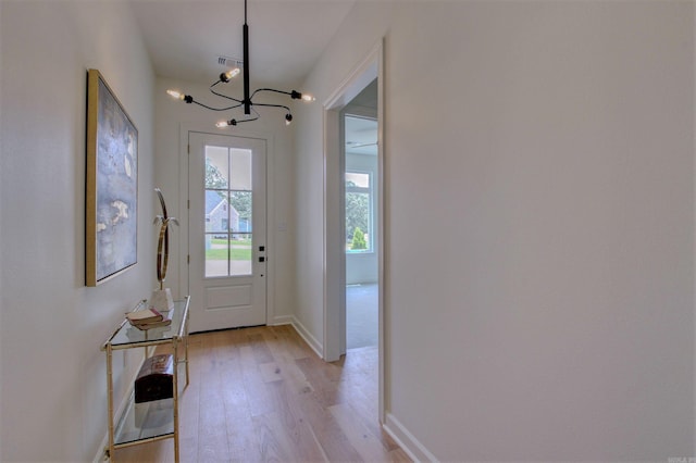 doorway to outside featuring light wood-style flooring, visible vents, baseboards, and a notable chandelier