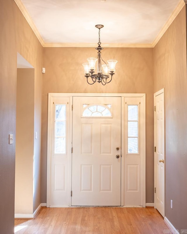 entryway with ornamental molding, a notable chandelier, light wood-style flooring, and baseboards