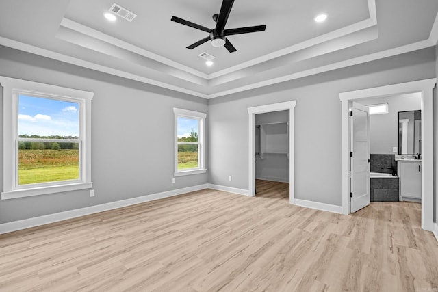 unfurnished bedroom with light wood-style floors, a tray ceiling, visible vents, and baseboards