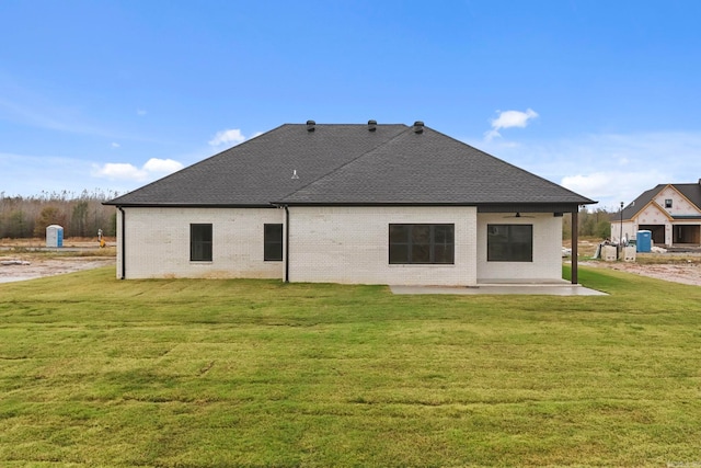 rear view of house with a patio, brick siding, a lawn, and a shingled roof