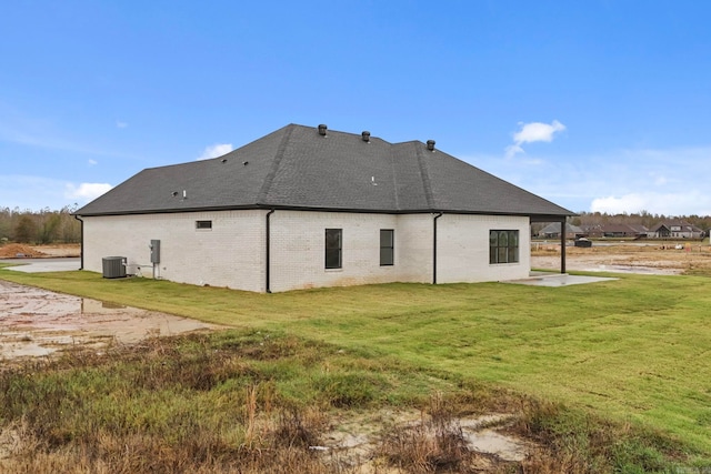 back of property with brick siding, roof with shingles, cooling unit, and a yard