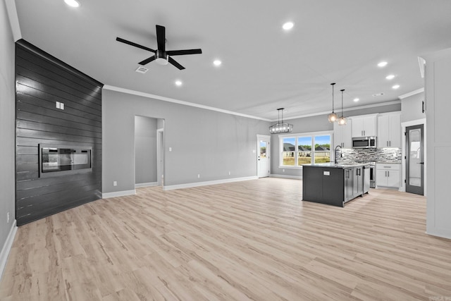 unfurnished living room featuring ornamental molding, a fireplace, light wood-style flooring, and ceiling fan with notable chandelier