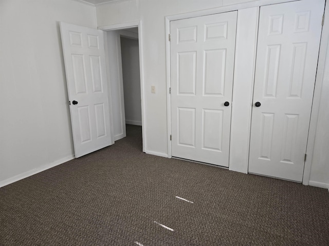 unfurnished bedroom with dark colored carpet, a closet, and baseboards