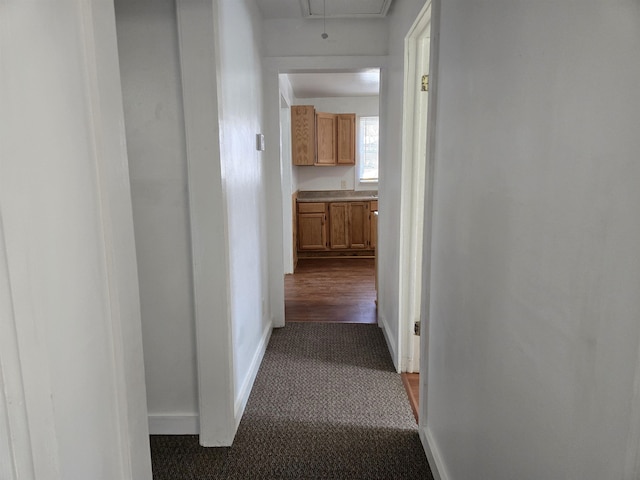 corridor featuring dark carpet, attic access, and baseboards