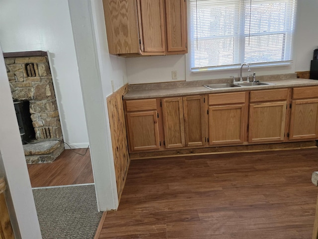 kitchen featuring a sink, light countertops, a stone fireplace, and dark wood finished floors