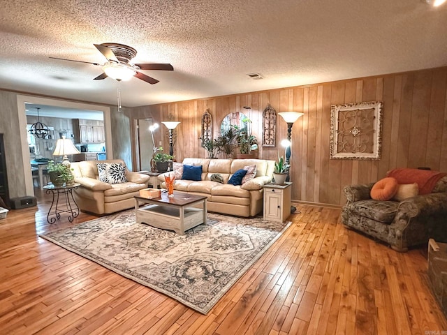 living room featuring visible vents, a textured ceiling, light wood-style flooring, and a ceiling fan