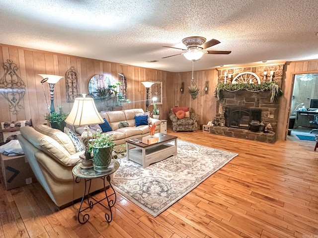 living area with wood-type flooring, a fireplace, ceiling fan, and a textured ceiling