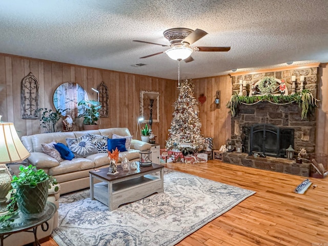 living area featuring ceiling fan, a stone fireplace, a textured ceiling, and wood finished floors