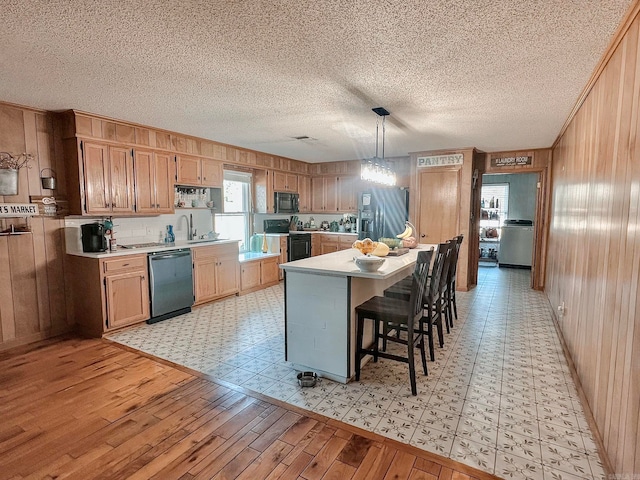 kitchen featuring wooden walls, light wood-style flooring, a breakfast bar, light countertops, and black appliances