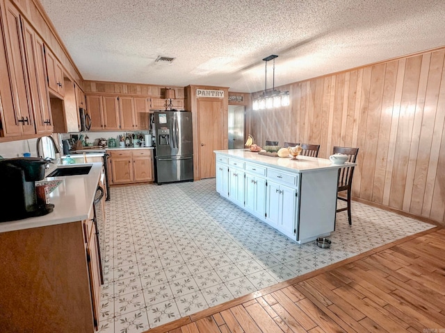 kitchen featuring light countertops, hanging light fixtures, visible vents, light wood-type flooring, and black fridge