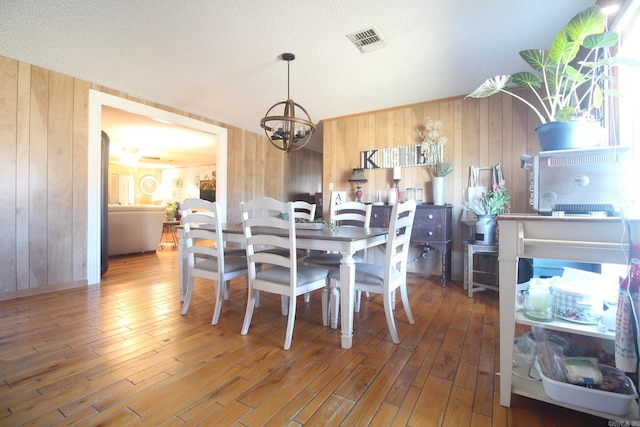 dining space with wooden walls, hardwood / wood-style flooring, visible vents, and a notable chandelier