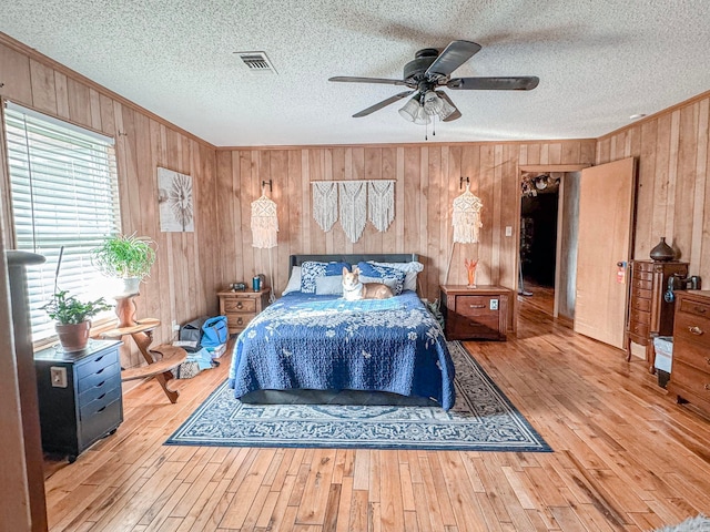 bedroom featuring visible vents, ornamental molding, wood walls, a textured ceiling, and hardwood / wood-style flooring