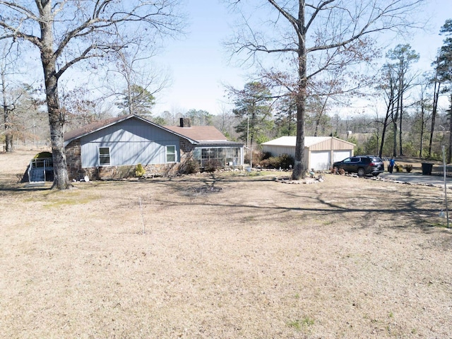 view of front of house with stone siding, a detached garage, a chimney, and an outbuilding