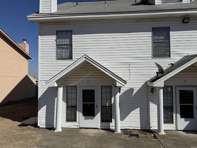 property entrance with a shingled roof and a patio area