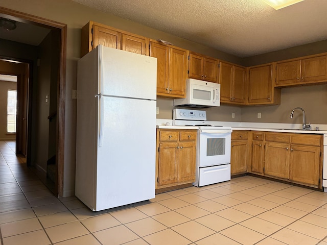 kitchen featuring light countertops, light tile patterned flooring, a sink, a textured ceiling, and white appliances