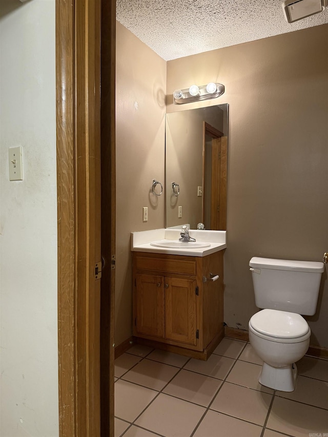 half bath featuring toilet, a textured ceiling, vanity, baseboards, and tile patterned floors