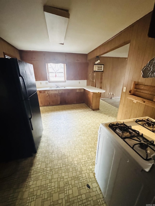 kitchen featuring wooden walls, a peninsula, light countertops, freestanding refrigerator, and range with gas cooktop