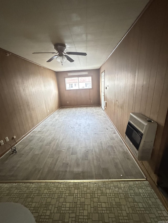 unfurnished room with a ceiling fan, wooden walls, heating unit, and wood finished floors