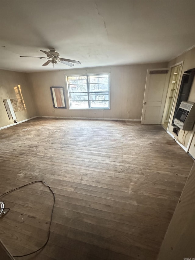 unfurnished living room with baseboards, ceiling fan, heating unit, and wood finished floors