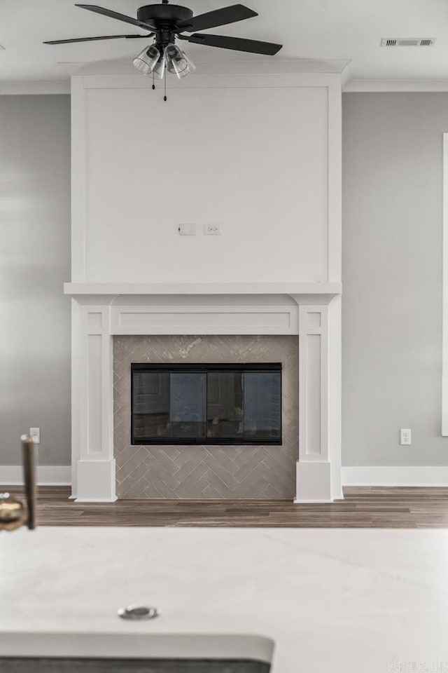 interior details with visible vents, wood finished floors, crown molding, and a glass covered fireplace