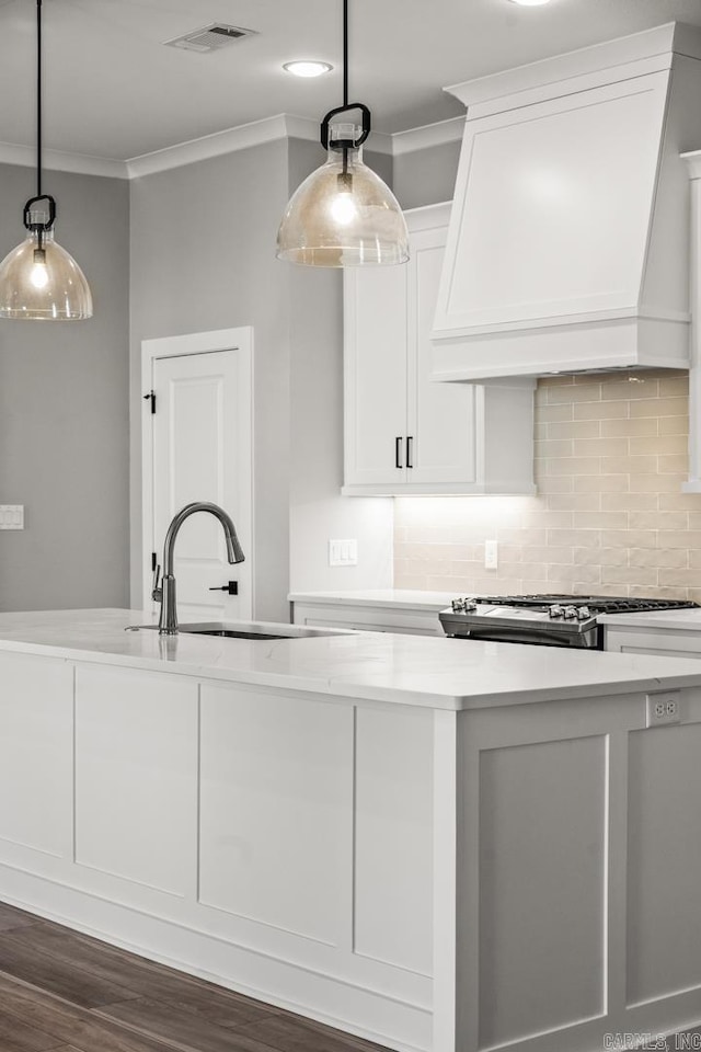 kitchen featuring visible vents, decorative backsplash, custom range hood, light countertops, and a sink