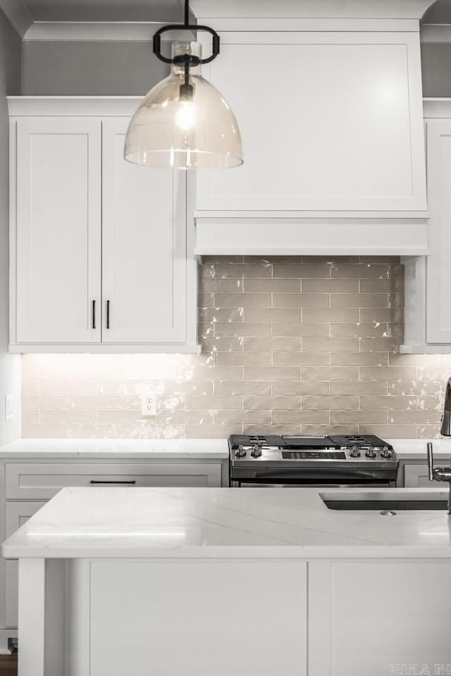 kitchen featuring stainless steel gas range, white cabinets, and decorative backsplash