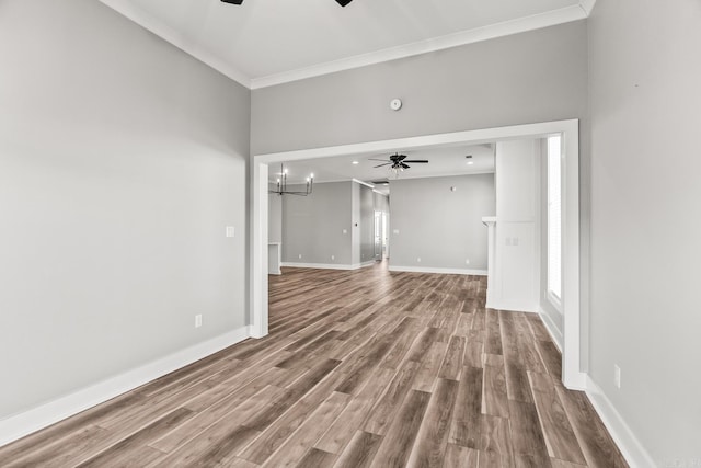 unfurnished living room with ceiling fan with notable chandelier, ornamental molding, wood finished floors, and baseboards