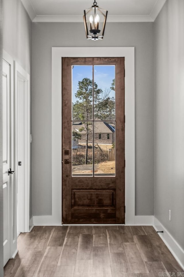 doorway to outside with an inviting chandelier, baseboards, ornamental molding, and wood finished floors