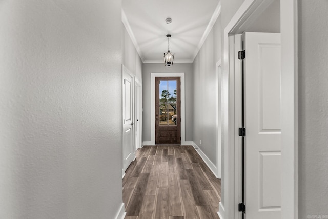 doorway with baseboards, a textured wall, dark wood-type flooring, crown molding, and a notable chandelier